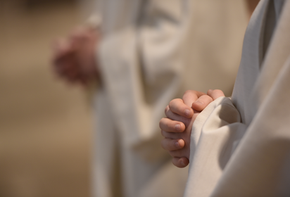 Zu sehen sind weiße liturgische Gewänder und zum Gebet gefaltete Hände